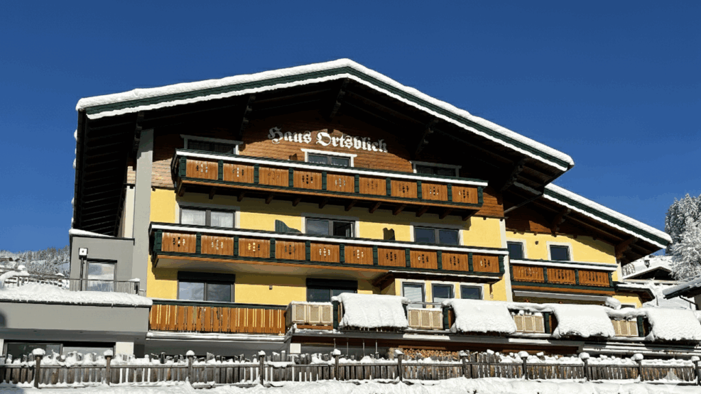 Deutsch: Man sieht das Haus Ortsblick im alpinen Stil, umgeben von schneebedecktem Gelände. Die Sonne scheint auf das Haus und verleiht der Szenerie Wärme und Gemütlichkeit.
English: You can see the Haus Ortsblick in alpine style, surrounded by snow-covered terrain. The sun shines on the house, lending warmth and coziness to the scene.